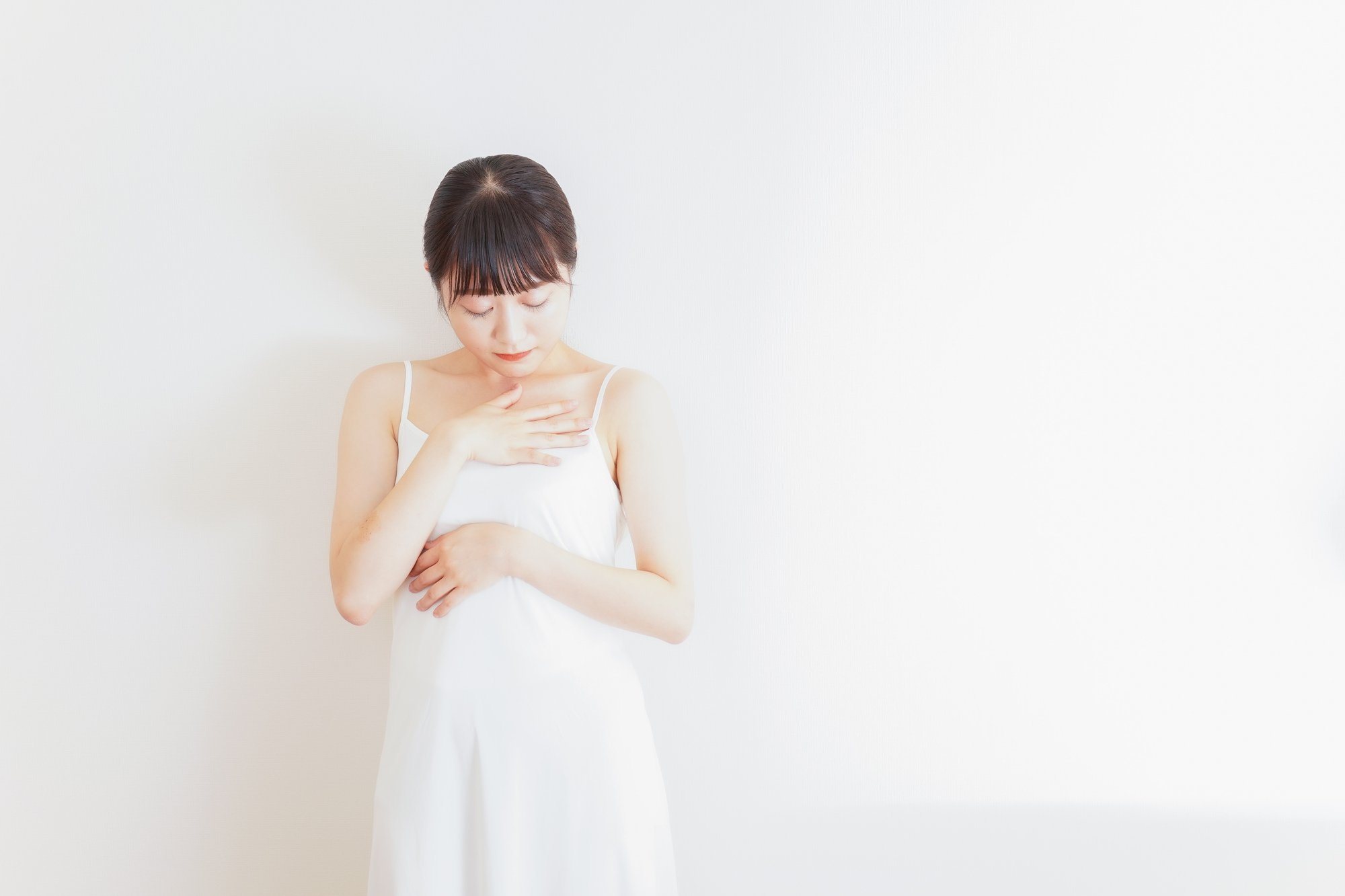 俯き胸元を抱えるように触っている女性