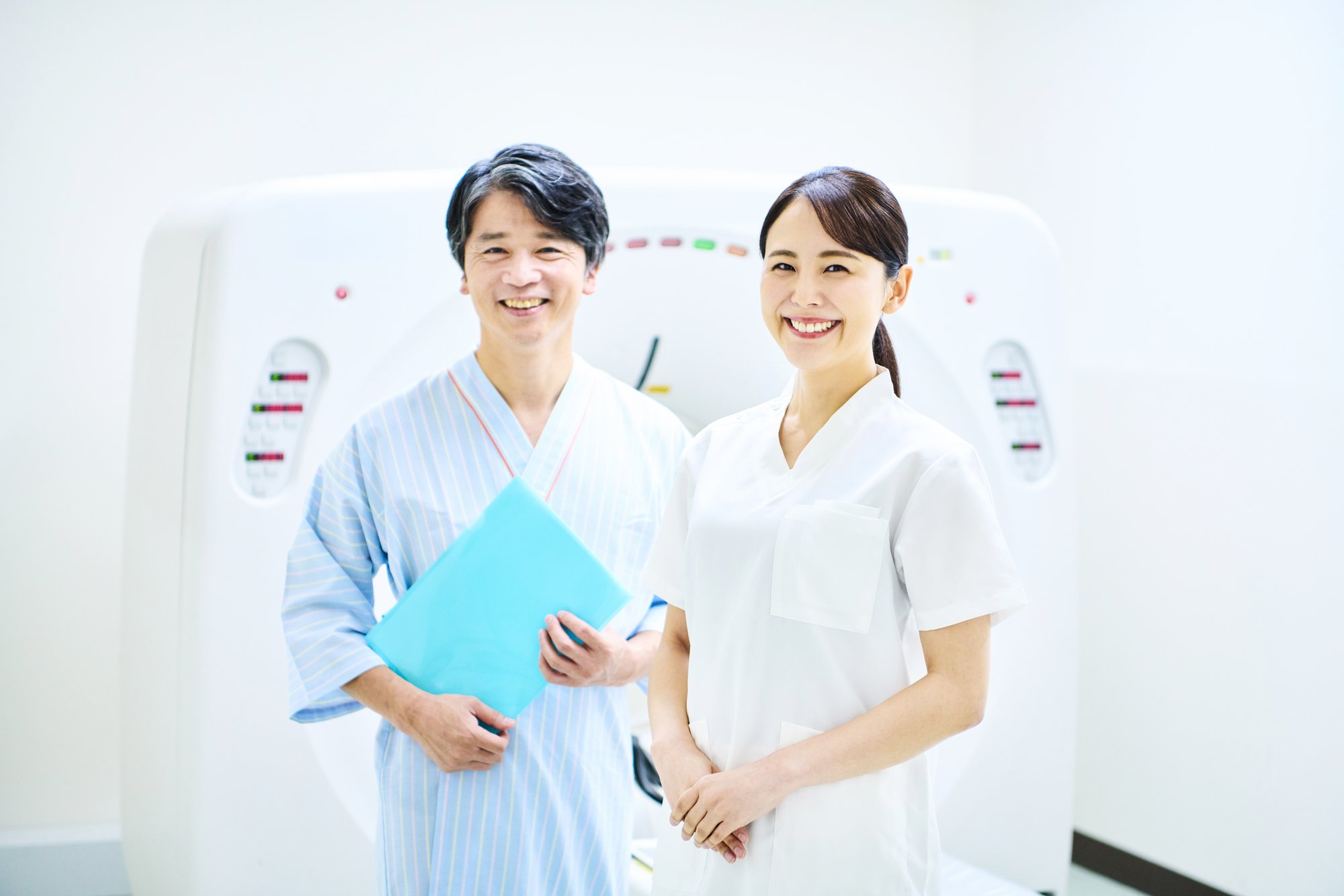 検査機器の前に立っている検査着を着てファイルを持った男性と女性看護師.jpg