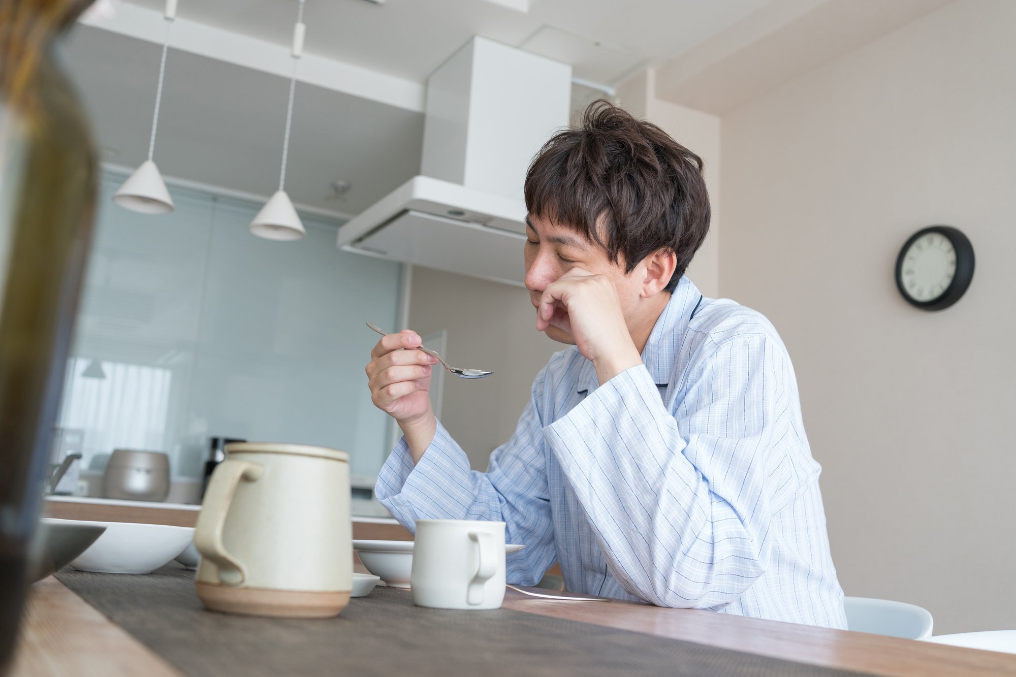 目を擦りながら寝間着で食事をする男性
