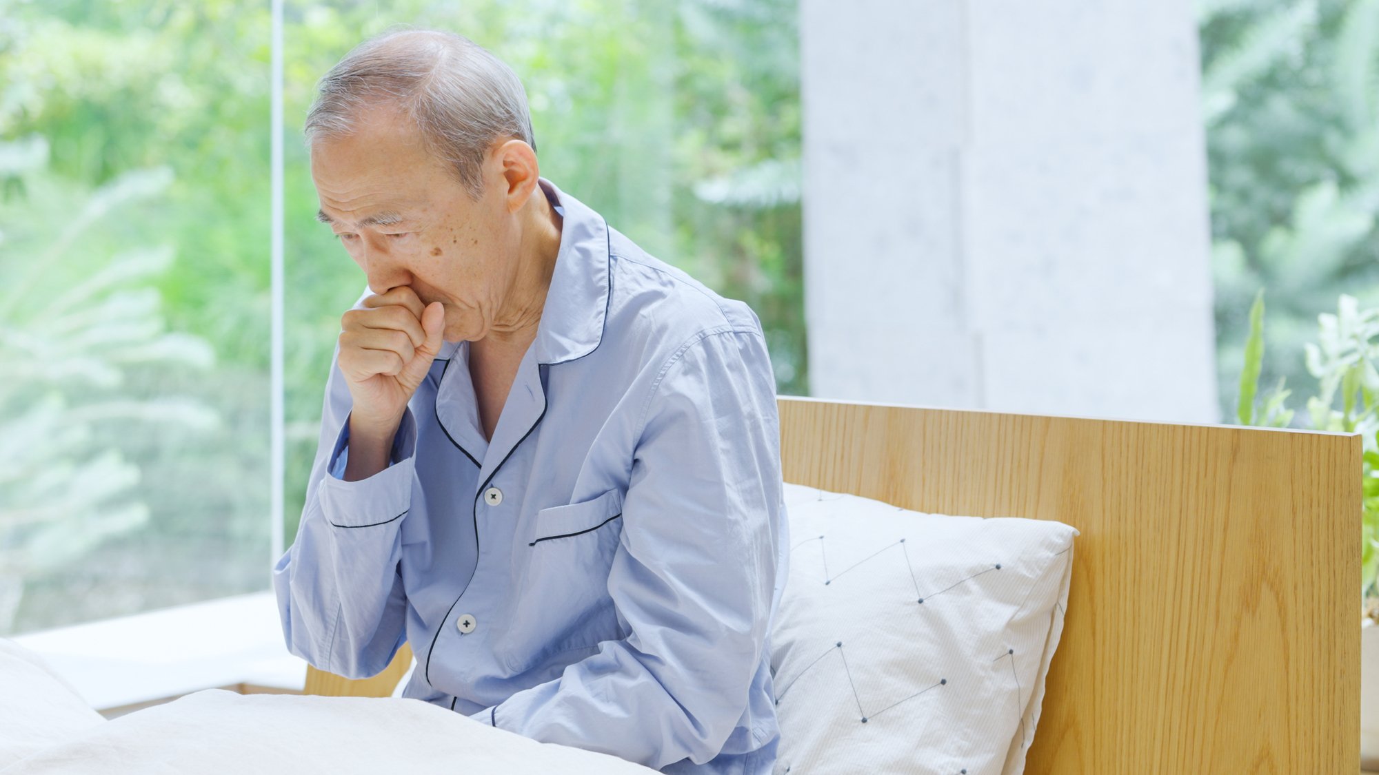 入院しておりベッドで咳をしている高齢男性.jpg
